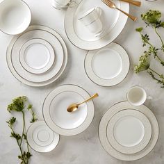 a table set with white plates and silverware next to greenery on the table