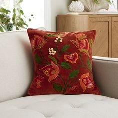 a red pillow with flowers on it sitting on a white couch in front of a window