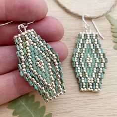 a pair of green and white beaded earrings sitting on top of a wooden table