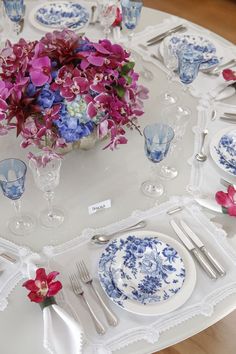 the table is set with blue and white plates, silverware, and pink flowers