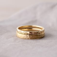 two gold wedding rings sitting on top of a white cloth covered bed sheet, with one ring in the middle