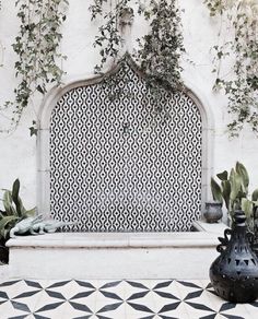 a black and white tiled fountain with potted plants next to it in front of a wall