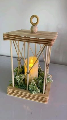 a lit candle in a wooden cage with greenery