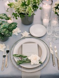 the table is set with white flowers and silverware