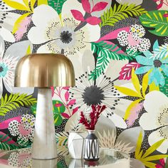 a lamp on a table in front of a wallpapered with flowers and leaves