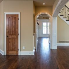 an empty hallway with wood floors and white trim on the walls, along with a wooden door that leads to another room