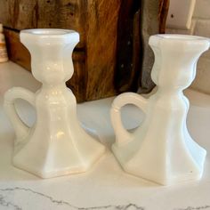 two white glass candlesticks sitting on top of a counter