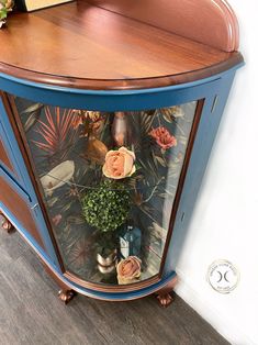 a blue corner cabinet with flowers and plants in it's glass door display case