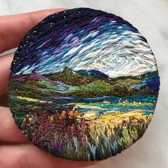 a hand holding a small round piece of art that looks like it has been painted