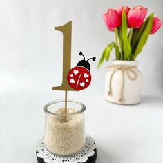 a table topped with a glass jar filled with rice and a cake topper that has a ladybug on it