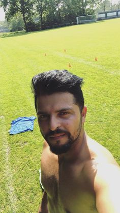 a man with no shirt on posing for the camera in front of a soccer field