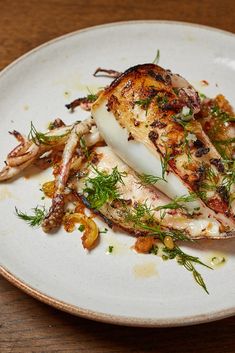 a white plate topped with chicken covered in sauce and garnishes on top of a wooden table