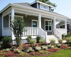 a house with flowers in the front yard and landscaping on the lawn around it's porch