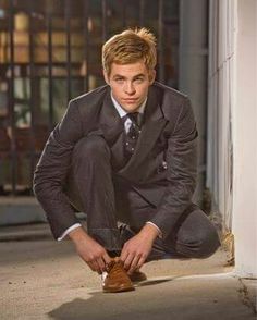 a young man in a suit and tie tying his shoe on the street at night