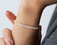 a woman's arm with a white beaded bracelet on top of her wrist