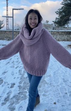 a woman is walking in the snow with her arms spread out and she is wearing a purple sweater