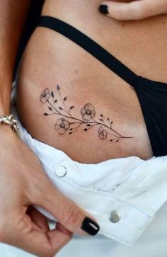 a woman's stomach with flowers and leaves tattooed on the side of her belly