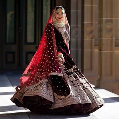 a woman in a red and black bridal gown is walking down the street with her hand on her hip