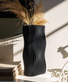 a tall black vase sitting on top of a table next to a book and plant