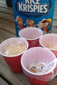 four red cups filled with cereal sitting on top of a wooden table next to a box of krispy kreme