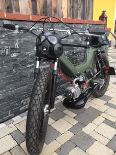 a green motorcycle parked next to a brick wall with a black handlebar on it