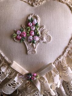 a heart shaped pillow with pink flowers on the front and white lace trim around it