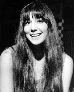 a black and white photo of a woman with long hair smiling in front of a wall