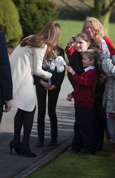 a woman holding a stuffed animal standing next to a little boy in front of a group of people