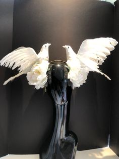 a black vase with white flowers in it and two birds perched on the top one