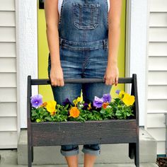 a woman standing in front of a door holding a planter with flowers on it