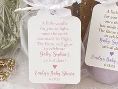 two baby shower gift tags sitting on top of a lace covered table next to a glass vase