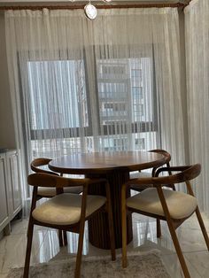 a dining room table with four chairs in front of a window covered by sheer curtains