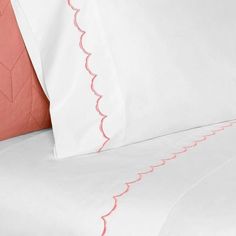 a bed with white sheets and pink trimmings on the headboard, along with an orange pillow case