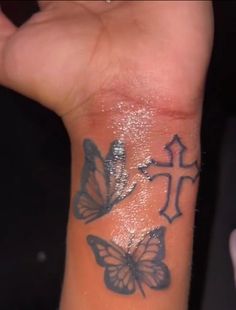 a person with a butterfly tattoo on their wrist holding up the cross and two butterflies