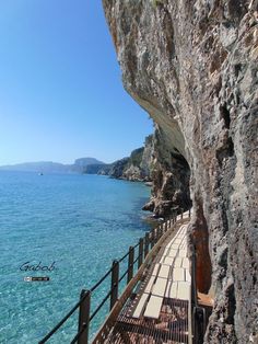 a wooden walkway next to the ocean on a sunny day with clear blue water and mountains in the background