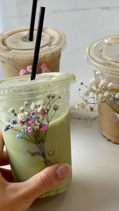 a hand holding a drink in front of two cups with straws and flowers on them