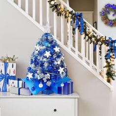 a blue christmas tree with presents under the banister