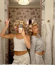 two women standing in front of a bathroom mirror with hair dryers on their heads