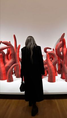 a woman standing in front of an art work on display with red sculptures behind her