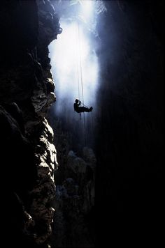 a man hanging from a rope in the middle of a cave with sunlight streaming through