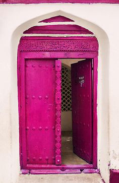 an open red door on the side of a white building with purple trimmings