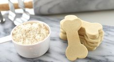 a dog bone shaped cookie next to a small bowl of powdered sugar on a marble table