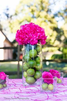 a vase filled with green apples and pink flowers on top of a purple table cloth