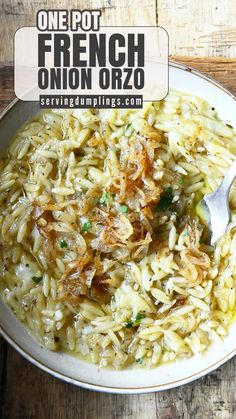 a white bowl filled with pasta and meat on top of a wooden table next to a spoon