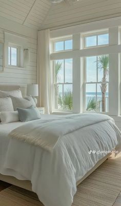 a large white bed sitting in a bedroom next to two windows with palm trees on them