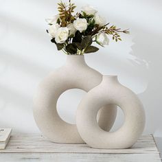 a white vase with flowers in it sitting on a table next to a stack of books