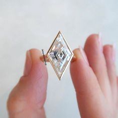 a person is holding a ring with a square shaped diamond in it's middle