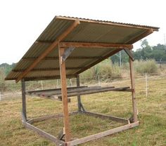 a wooden structure with a metal roof in the middle of a field