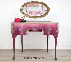 a pink desk with a mirror on top of it next to a white wall and wooden floor