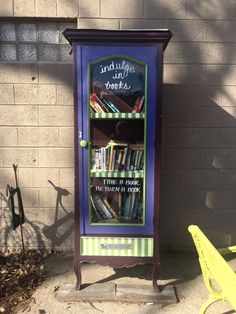 a purple bookcase with books on it sitting next to a yellow chair and a brick wall